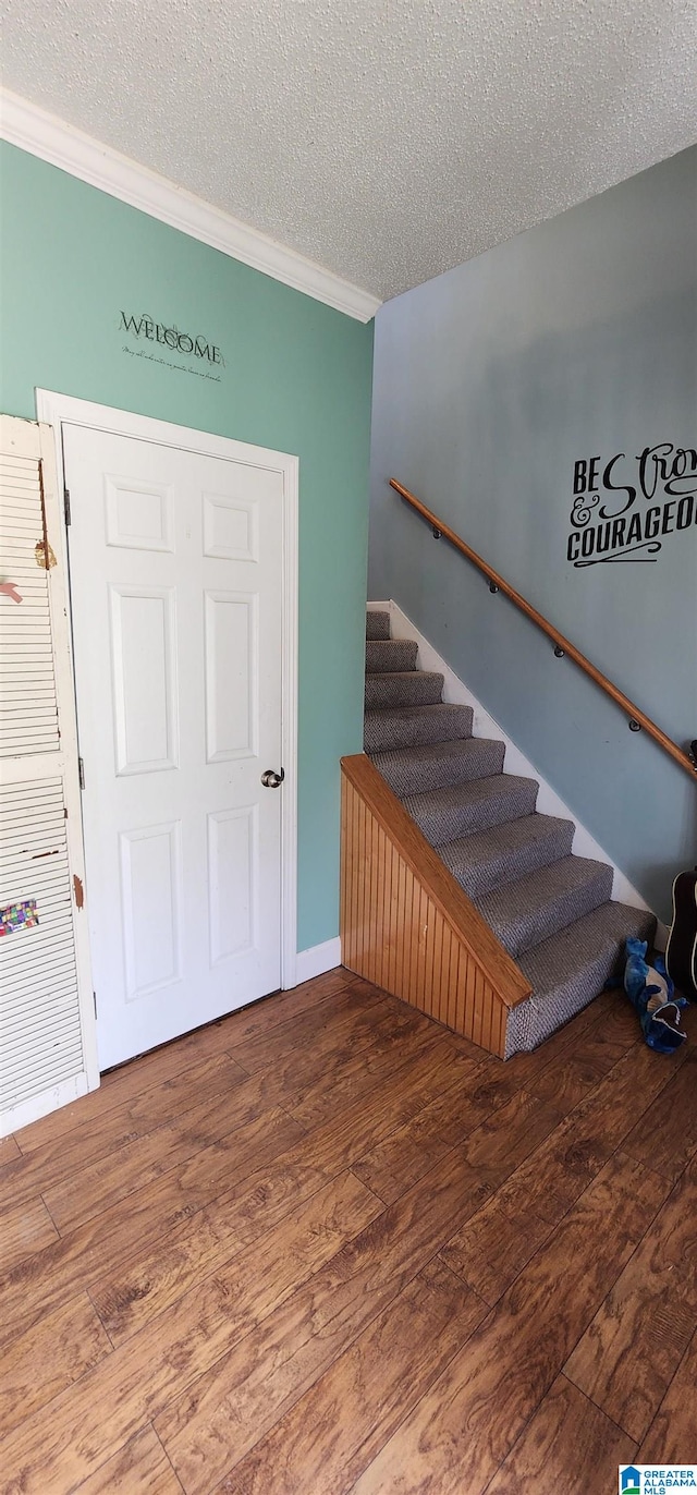 stairs with crown molding, a textured ceiling, and hardwood / wood-style floors