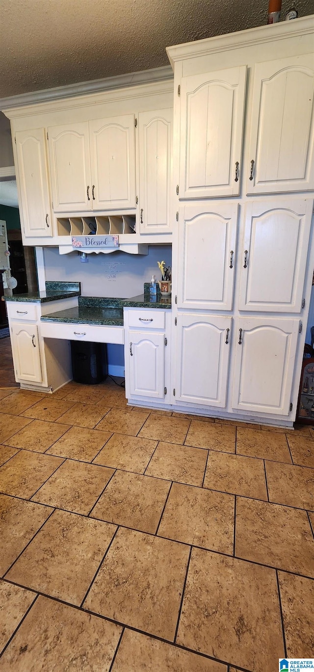 kitchen with built in desk, a textured ceiling, light tile floors, wall chimney range hood, and white cabinets