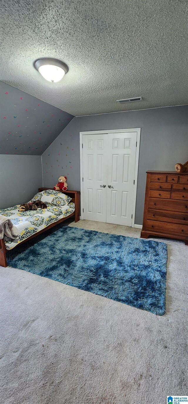 unfurnished bedroom featuring lofted ceiling, a closet, a textured ceiling, and carpet flooring