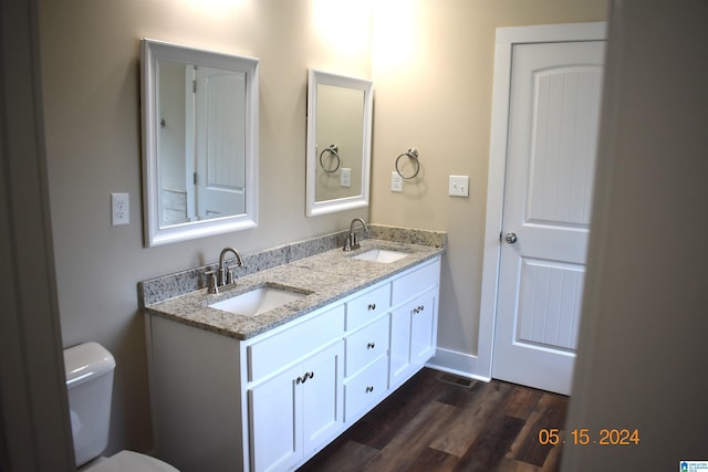 bathroom with toilet, vanity with extensive cabinet space, double sink, and hardwood / wood-style flooring