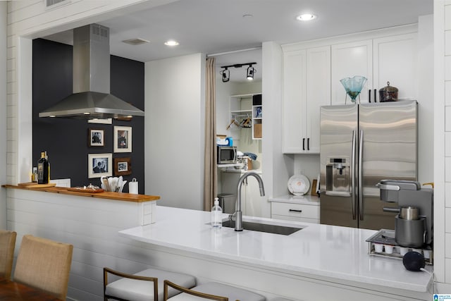 kitchen with a kitchen breakfast bar, white cabinetry, wall chimney exhaust hood, sink, and appliances with stainless steel finishes