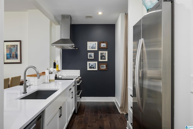 kitchen featuring dark wood-type flooring, wall chimney range hood, sink, white cabinetry, and appliances with stainless steel finishes