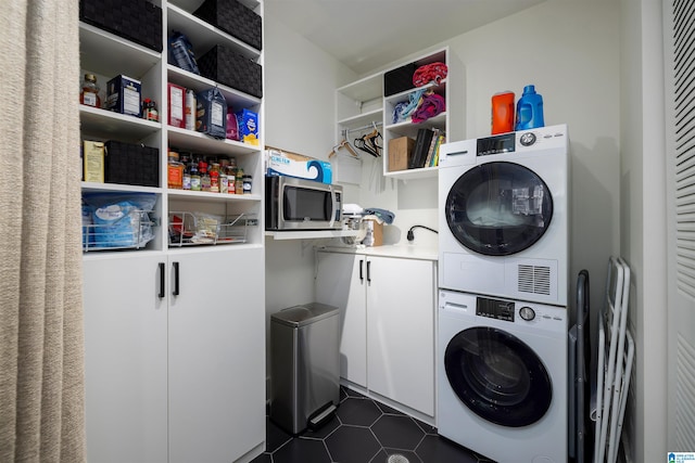 washroom featuring cabinets, dark tile flooring, and stacked washer / drying machine