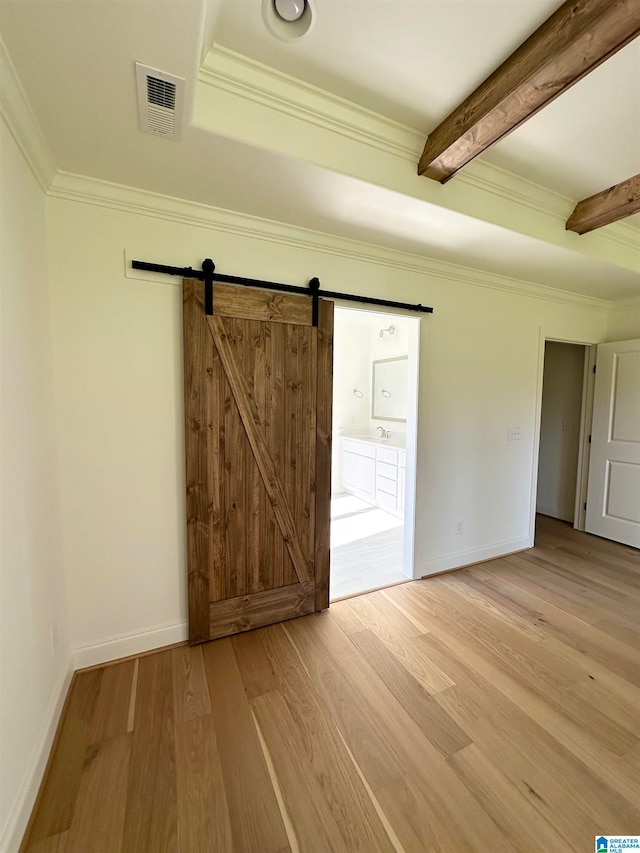 spare room featuring beamed ceiling, a barn door, light hardwood / wood-style flooring, and crown molding