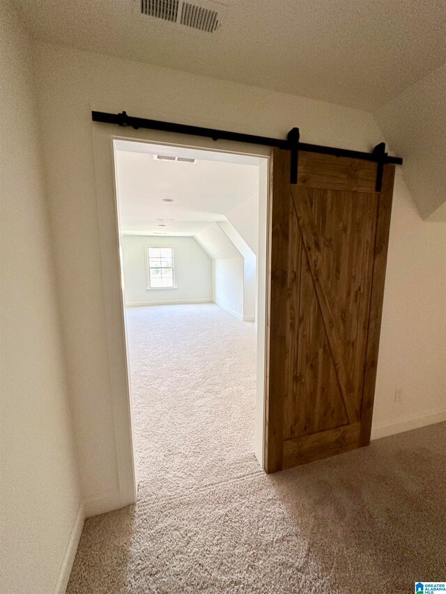 hallway featuring a barn door, carpet, and lofted ceiling