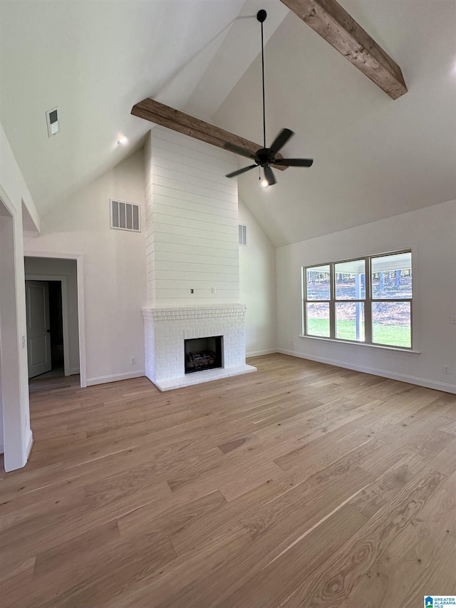 unfurnished living room featuring ceiling fan, a brick fireplace, beam ceiling, and light hardwood / wood-style flooring