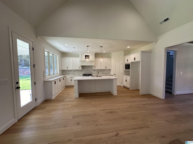 kitchen featuring pendant lighting, built in microwave, an island with sink, sink, and white cabinets