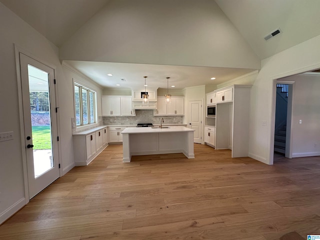 kitchen with pendant lighting, built in microwave, sink, white cabinets, and a kitchen island with sink