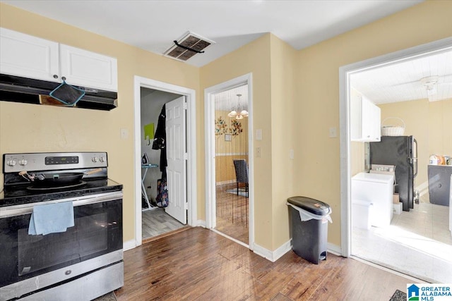 kitchen with black fridge, stainless steel range with electric cooktop, an inviting chandelier, white cabinets, and hardwood / wood-style floors