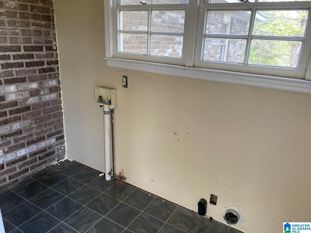 washroom with dark tile flooring, washer hookup, and brick wall