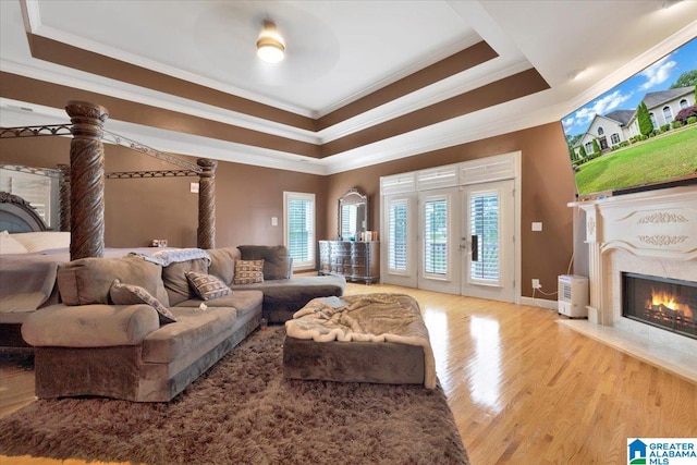 living room featuring a premium fireplace, french doors, crown molding, light wood-type flooring, and a raised ceiling