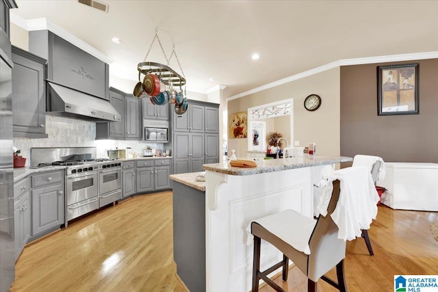 kitchen featuring wall chimney exhaust hood, appliances with stainless steel finishes, light wood-type flooring, and gray cabinets