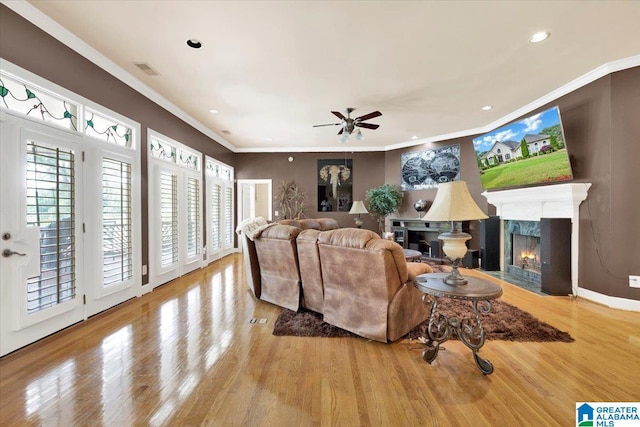 living room with light hardwood / wood-style floors, ceiling fan, crown molding, and a high end fireplace