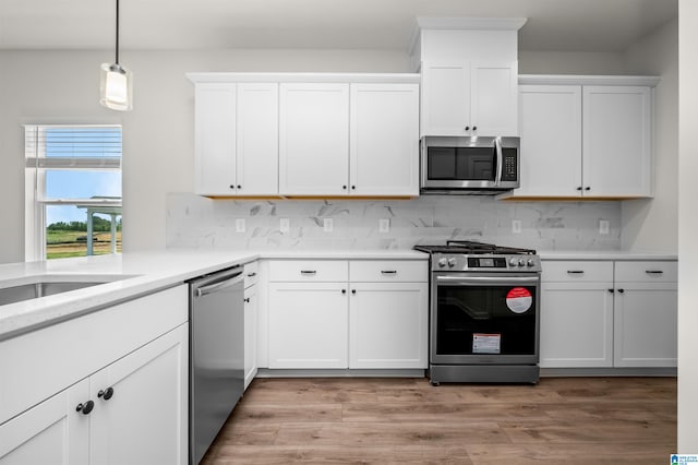 kitchen featuring white cabinetry, stainless steel appliances, decorative backsplash, pendant lighting, and light hardwood / wood-style flooring