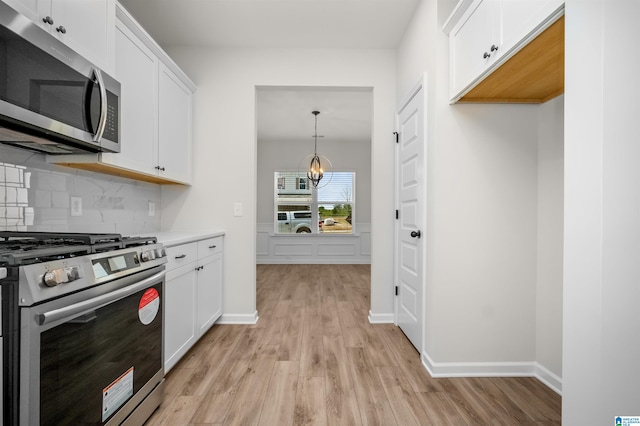 kitchen with light wood-type flooring, stainless steel appliances, white cabinets, and hanging light fixtures