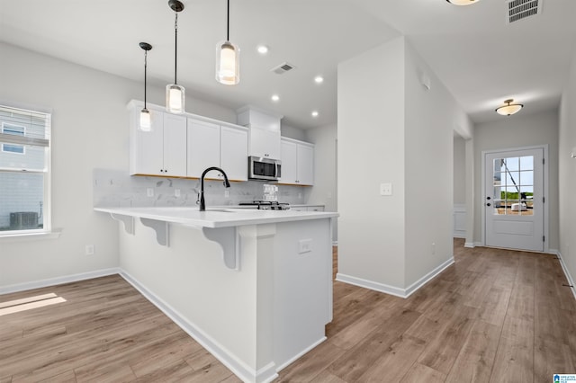 kitchen featuring a kitchen bar, backsplash, decorative light fixtures, light wood-type flooring, and white cabinets