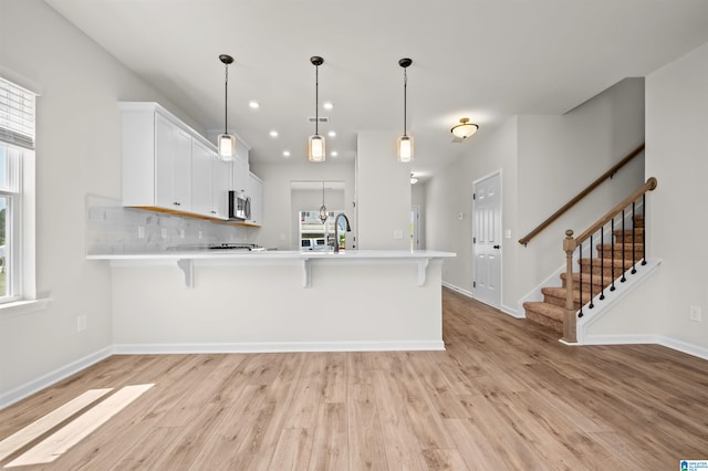 kitchen with kitchen peninsula, a kitchen breakfast bar, light wood-type flooring, pendant lighting, and white cabinets