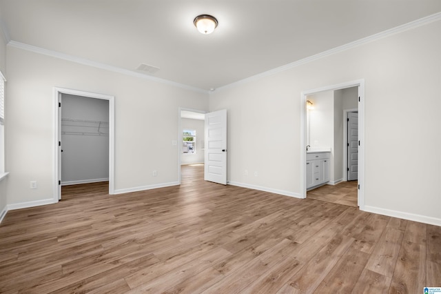 unfurnished bedroom with ensuite bathroom, light wood-type flooring, a spacious closet, ornamental molding, and a closet