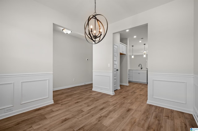 unfurnished dining area featuring sink, light wood-type flooring, and an inviting chandelier