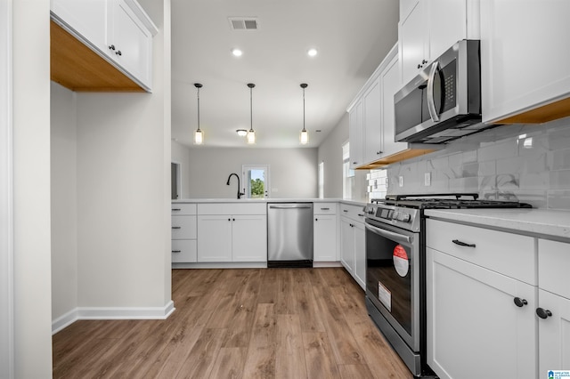 kitchen with decorative light fixtures, backsplash, sink, white cabinetry, and stainless steel appliances