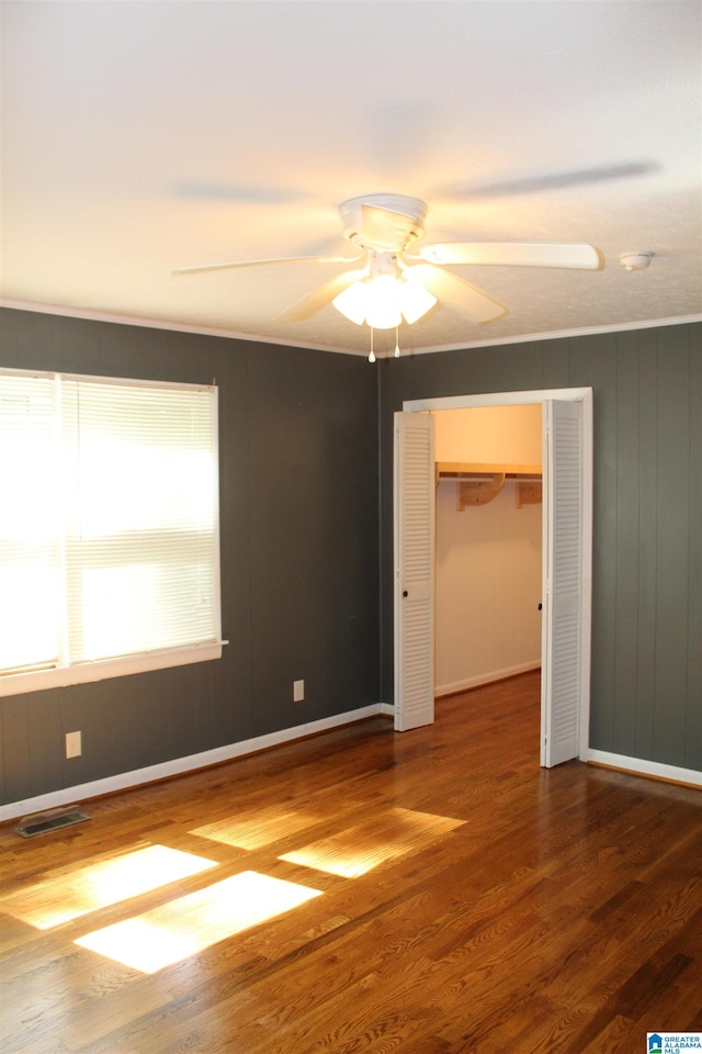 empty room featuring ornamental molding, dark wood-type flooring, and ceiling fan