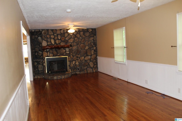 unfurnished living room with a textured ceiling, a stone fireplace, ceiling fan, and hardwood / wood-style floors