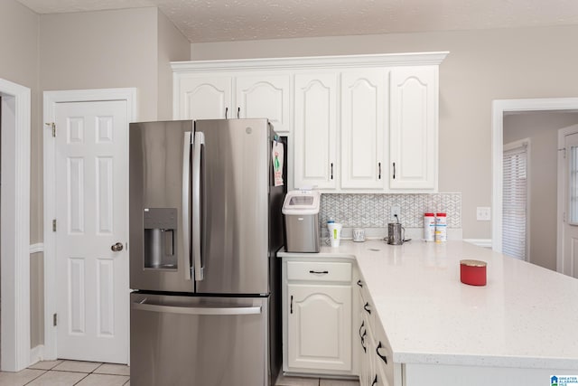 kitchen with white cabinets, stainless steel fridge, kitchen peninsula, and light tile patterned floors