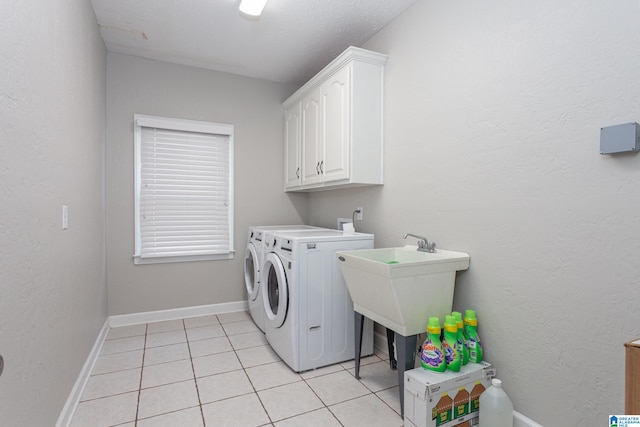 clothes washing area featuring cabinets, light tile patterned floors, and washing machine and clothes dryer