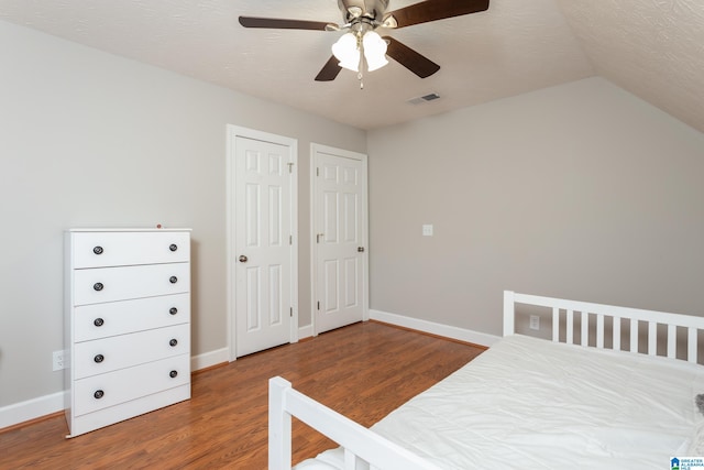 bedroom featuring ceiling fan, vaulted ceiling, a textured ceiling, two closets, and hardwood / wood-style flooring