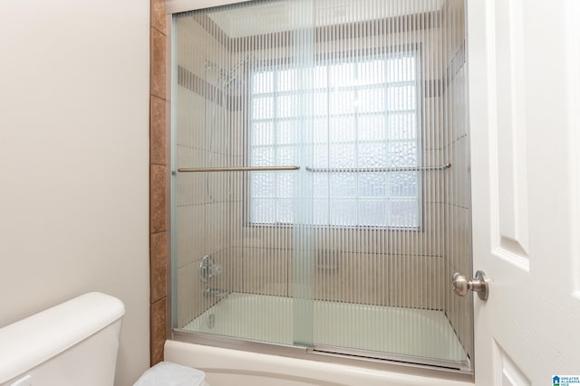 bathroom featuring combined bath / shower with glass door and toilet