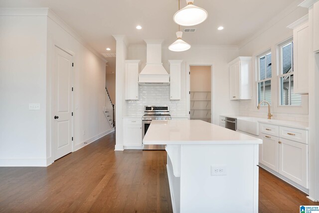 kitchen with stainless steel range oven, sink, hanging light fixtures, custom range hood, and white cabinets