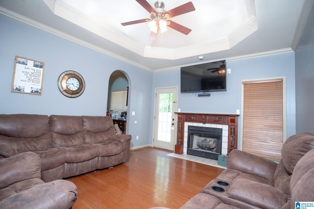 living room with a raised ceiling, ceiling fan, crown molding, and wood-type flooring