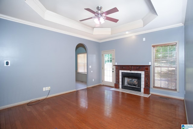 unfurnished living room with a healthy amount of sunlight, a tiled fireplace, hardwood / wood-style flooring, and a raised ceiling