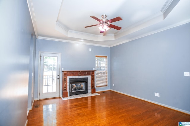 unfurnished living room featuring ornamental molding, hardwood / wood-style flooring, a tile fireplace, ceiling fan, and a raised ceiling