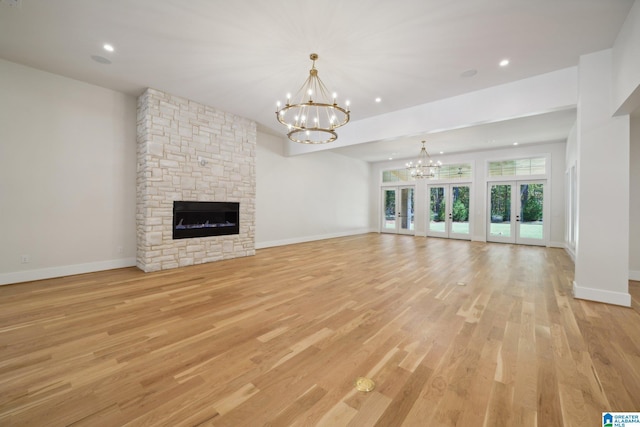 unfurnished living room with an inviting chandelier, a stone fireplace, light wood-type flooring, and french doors