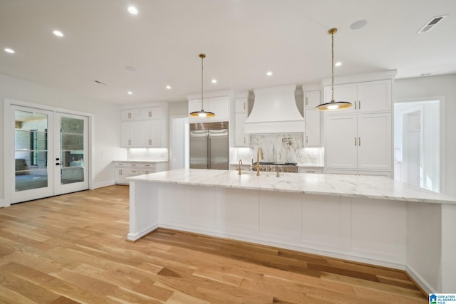 kitchen featuring premium range hood, a large island, stainless steel built in fridge, and white cabinets