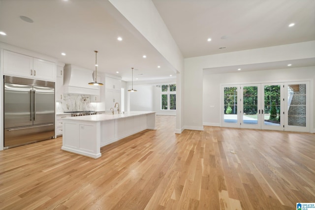 kitchen with premium range hood, stainless steel built in refrigerator, a spacious island, white cabinets, and hanging light fixtures