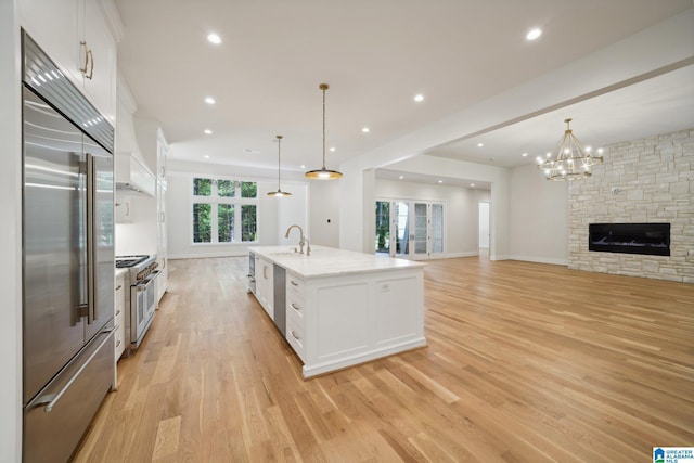 kitchen featuring pendant lighting, high end appliances, white cabinetry, and an island with sink