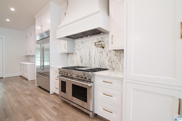 kitchen featuring light stone countertops, custom exhaust hood, high quality appliances, white cabinets, and light hardwood / wood-style floors