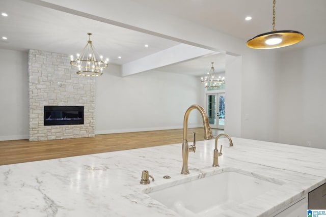 kitchen with light stone counters, sink, an inviting chandelier, a fireplace, and hardwood / wood-style floors