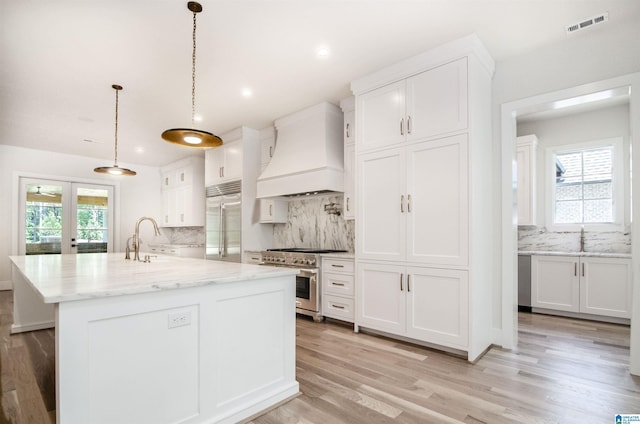 kitchen with white cabinetry, decorative light fixtures, a center island with sink, custom exhaust hood, and high end appliances