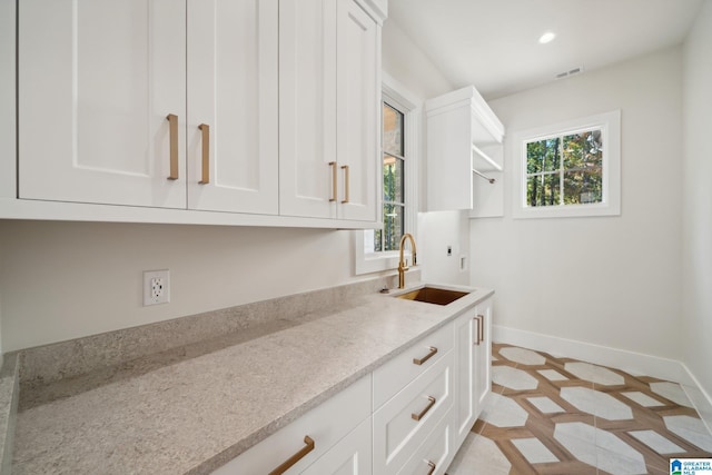 kitchen with white cabinets, light stone countertops, and sink