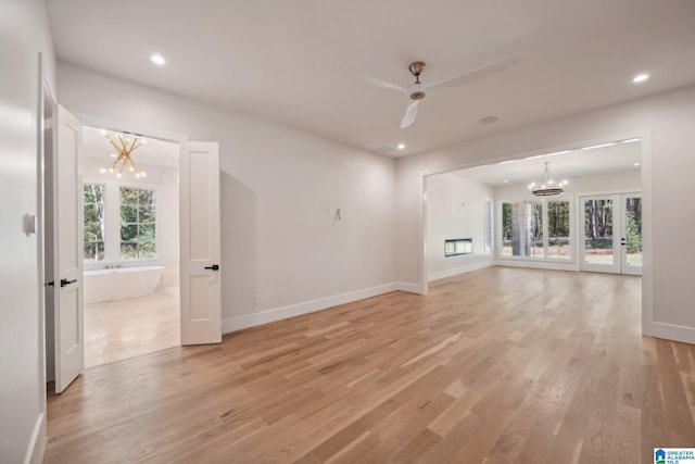 unfurnished living room featuring ceiling fan with notable chandelier, light hardwood / wood-style floors, a wealth of natural light, and french doors