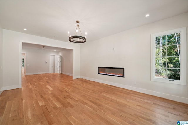 unfurnished living room with ceiling fan with notable chandelier and light wood-type flooring