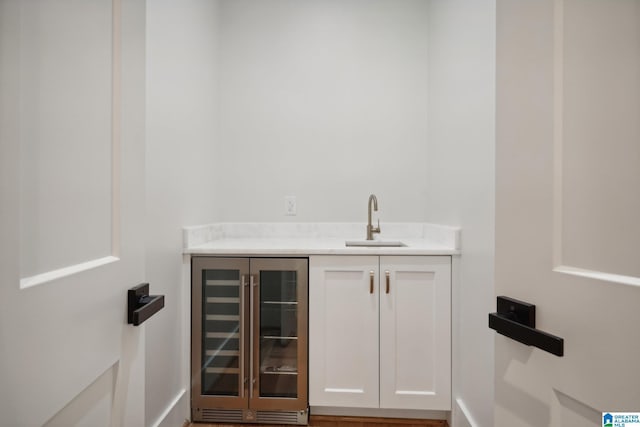 bar featuring white cabinets, beverage cooler, and sink