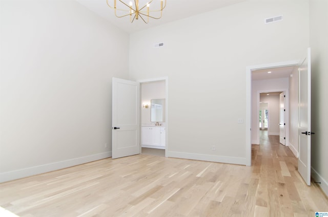 unfurnished bedroom with a towering ceiling, light hardwood / wood-style floors, and a notable chandelier