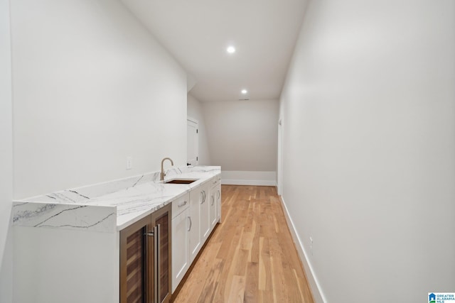 bar featuring light stone countertops, beverage cooler, sink, light hardwood / wood-style floors, and white cabinetry