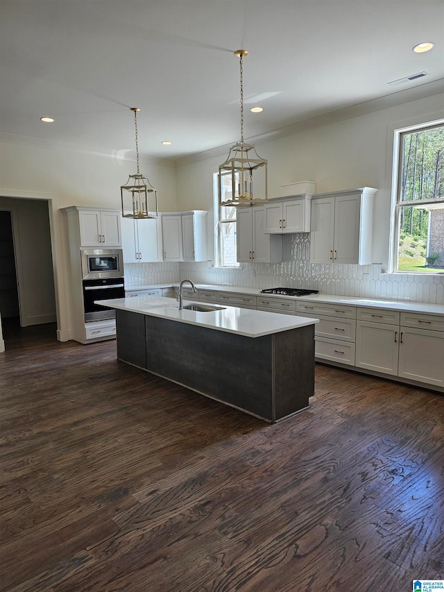 kitchen featuring stainless steel appliances, dark wood-type flooring, an island with sink, and decorative light fixtures