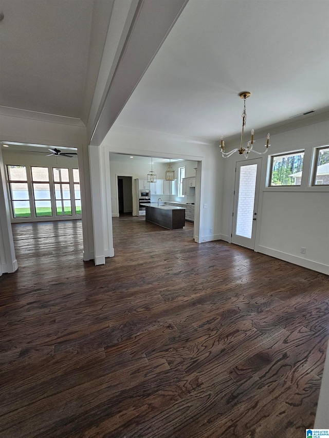 unfurnished living room featuring crown molding, ceiling fan with notable chandelier, and dark hardwood / wood-style flooring