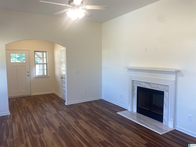 unfurnished living room featuring a premium fireplace, dark wood-type flooring, and ceiling fan